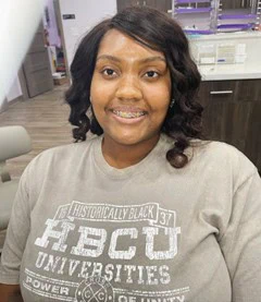 Smiling young woman with braces, wearing a "Historically Black Colleges and Universities" t-shirt, showcasing personalized orthodontic treatment at Imagine Orthodontic Studio.