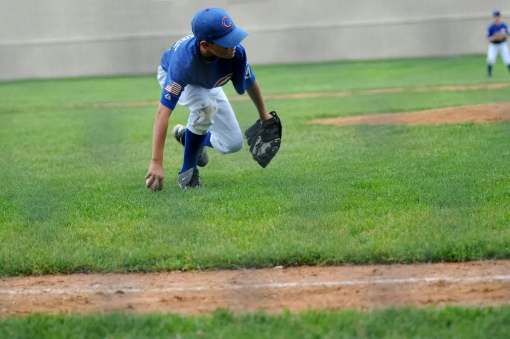 Young baseball player in blue uniform fielding the ball on grassy field, showcasing active participation in sports, relevant to orthodontic solutions for athletes.